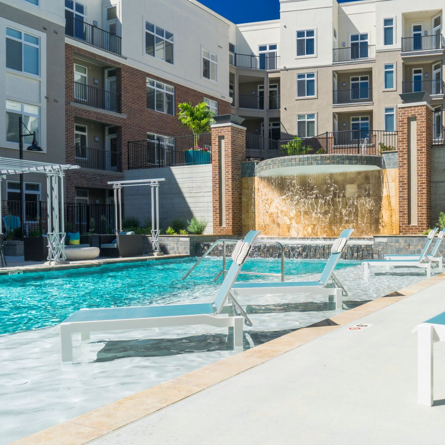 Domain City Center The building's balconies overlook the pool, adorned by planters and greenery, providing a relaxing environment under a clear blue sky.