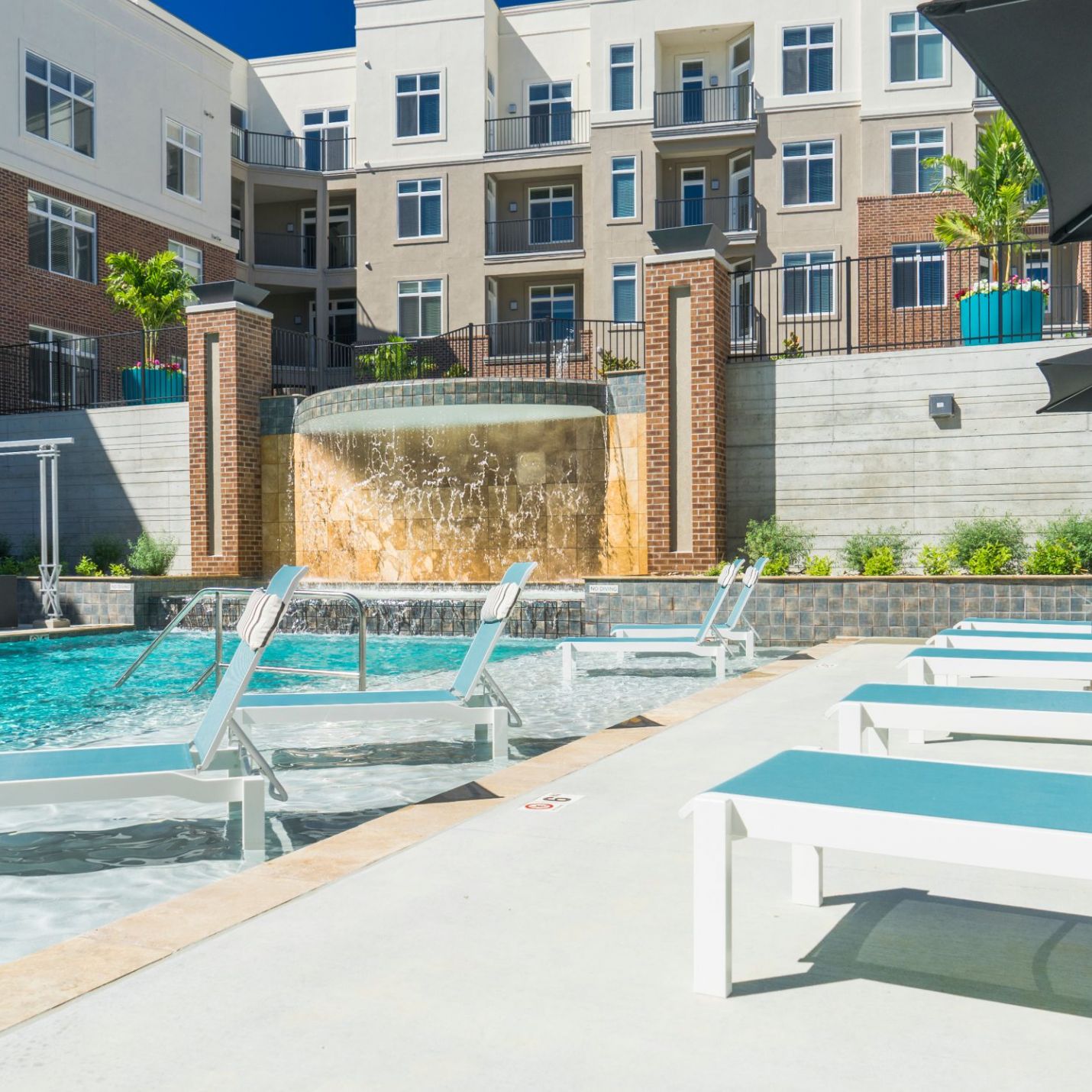 Domain City Center The building's balconies overlook the pool, adorned by planters and greenery, providing a relaxing environment under a clear blue sky.